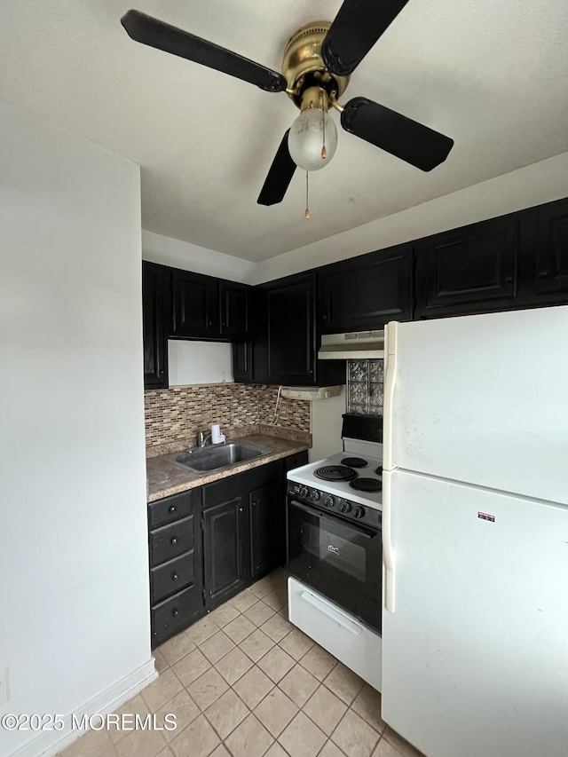 kitchen featuring electric range oven, freestanding refrigerator, dark cabinetry, under cabinet range hood, and a sink