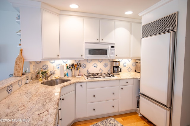 kitchen featuring backsplash, sink, paneled refrigerator, light stone countertops, and white cabinetry