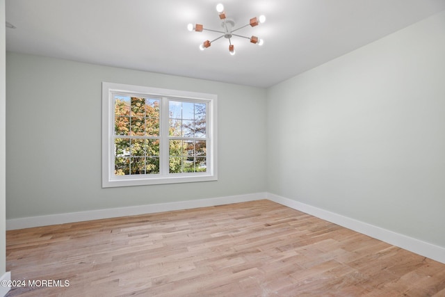 spare room with a chandelier and light wood-type flooring