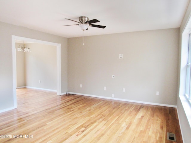 unfurnished room with a wealth of natural light, light hardwood / wood-style floors, and ceiling fan with notable chandelier