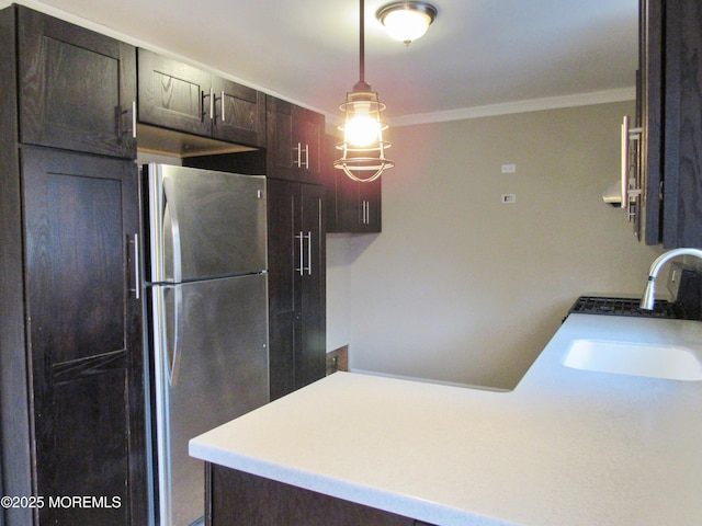 kitchen with dark brown cabinets, crown molding, sink, pendant lighting, and stainless steel refrigerator