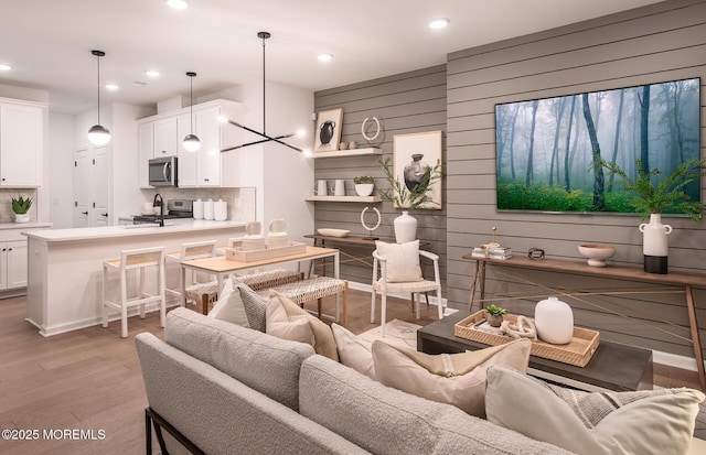 living room featuring wooden walls, sink, a notable chandelier, and light wood-type flooring