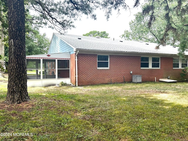 rear view of house with a yard, central AC unit, and a sunroom