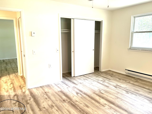 unfurnished bedroom featuring baseboard heating, light hardwood / wood-style flooring, and a closet