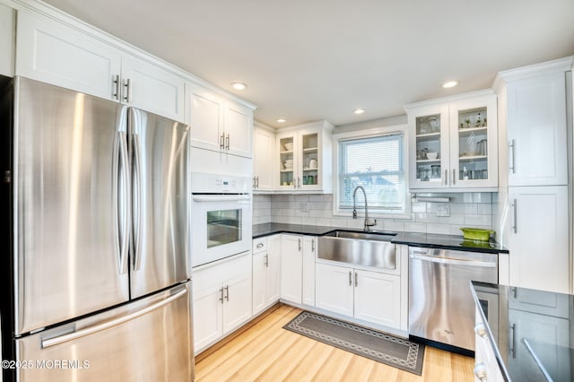 kitchen with sink, tasteful backsplash, appliances with stainless steel finishes, white cabinets, and light wood-type flooring