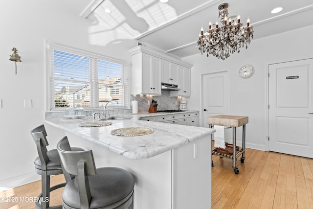 kitchen featuring white cabinetry, decorative backsplash, a kitchen breakfast bar, hanging light fixtures, and kitchen peninsula