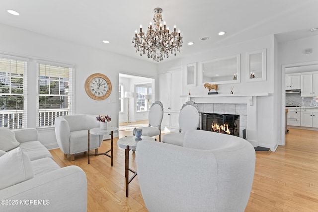 living room featuring a tile fireplace, light hardwood / wood-style floors, and a notable chandelier