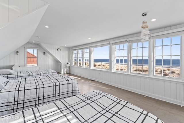 bedroom with hardwood / wood-style floors, lofted ceiling, a water view, and a view of the beach