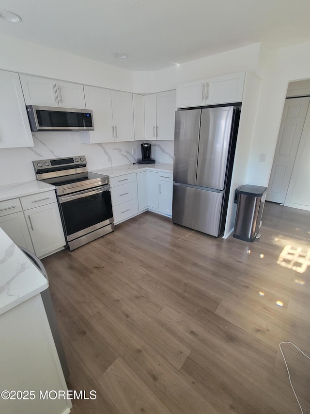 kitchen featuring appliances with stainless steel finishes, white cabinets, range hood, and wood-type flooring