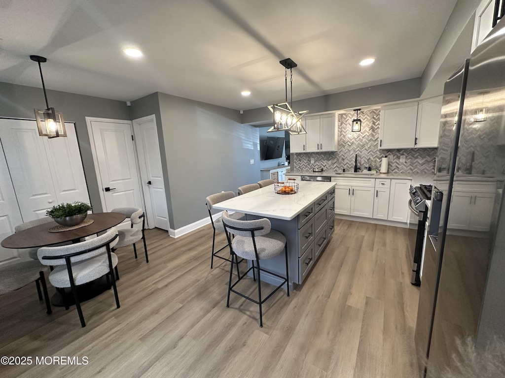 kitchen featuring a kitchen island, white cabinetry, a kitchen breakfast bar, hanging light fixtures, and light stone counters