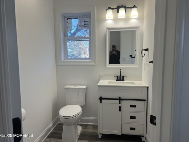 bathroom with toilet, vanity, baseboards, and wood finished floors