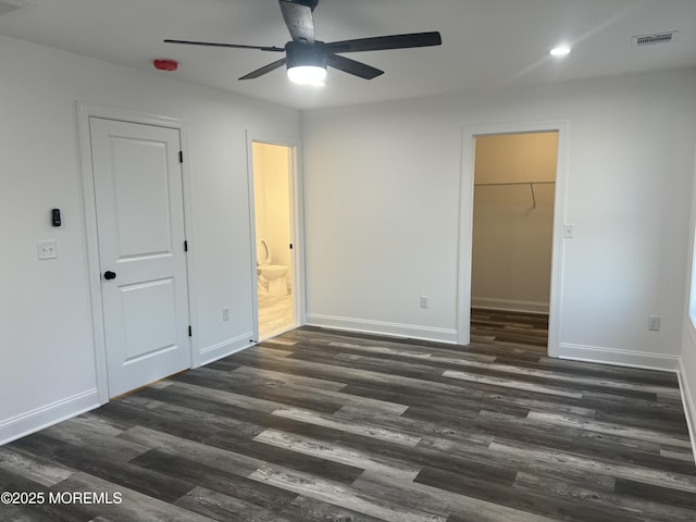 unfurnished bedroom with dark wood-style flooring, visible vents, baseboards, a closet, and a walk in closet