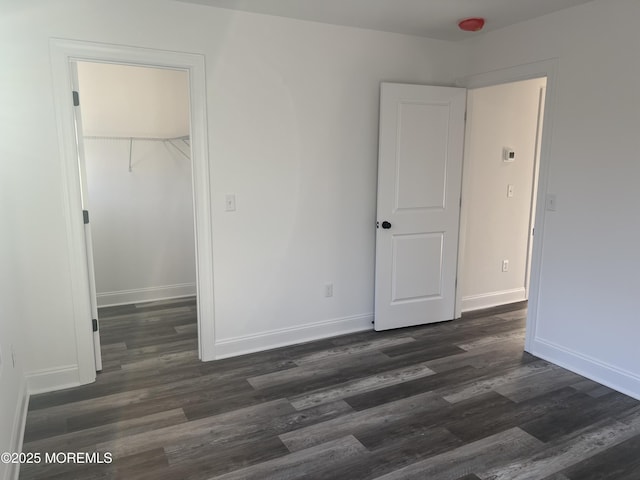 unfurnished bedroom featuring a closet, baseboards, a walk in closet, and dark wood-type flooring