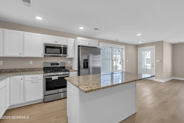 kitchen featuring appliances with stainless steel finishes, white cabinetry, light stone countertops, light hardwood / wood-style floors, and a kitchen island