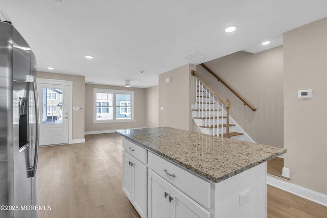 kitchen with white cabinets, stainless steel fridge, a center island, light stone counters, and light wood-type flooring