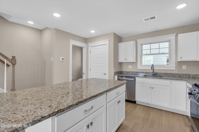 kitchen with sink, appliances with stainless steel finishes, light stone counters, white cabinets, and light wood-type flooring