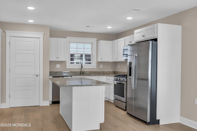 kitchen featuring light hardwood / wood-style flooring, appliances with stainless steel finishes, white cabinetry, a center island, and light stone countertops