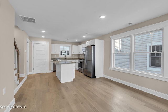 kitchen with sink, a center island, appliances with stainless steel finishes, light hardwood / wood-style floors, and white cabinets