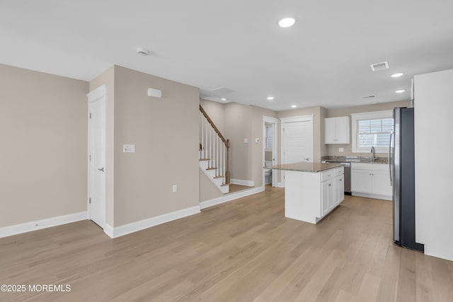 kitchen with a kitchen island, sink, white cabinets, stainless steel appliances, and light hardwood / wood-style flooring