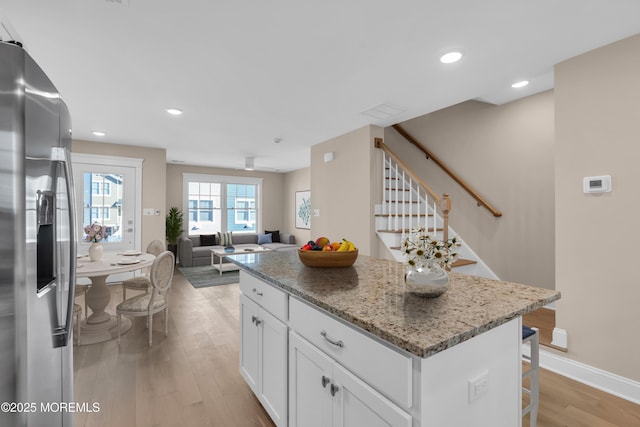 kitchen featuring stainless steel fridge, light stone counters, white cabinets, a kitchen island, and light wood-type flooring