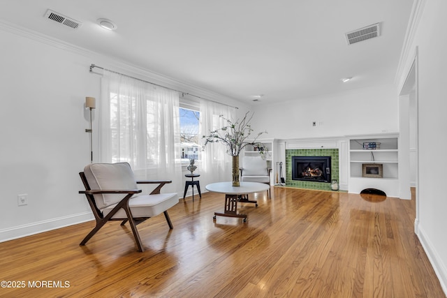 living area with a tiled fireplace, light wood-type flooring, built in shelves, and crown molding