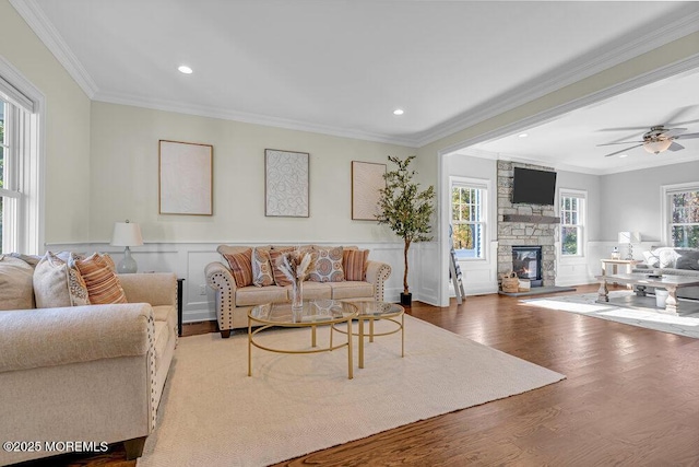 living room with hardwood / wood-style floors, a stone fireplace, crown molding, and a healthy amount of sunlight