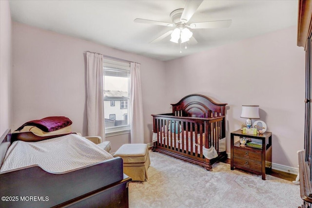 bedroom with ceiling fan, light carpet, and a nursery area