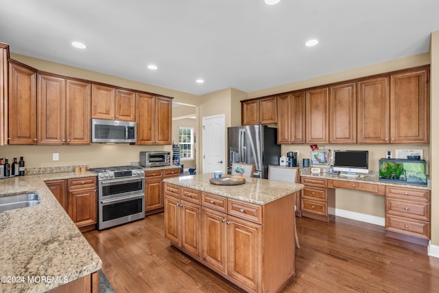 kitchen featuring stainless steel appliances, light stone counters, dark hardwood / wood-style floors, a kitchen island, and built in desk