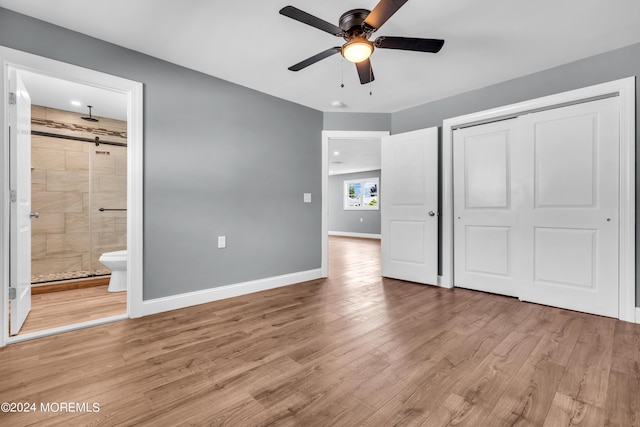 unfurnished bedroom featuring light hardwood / wood-style floors, a barn door, ceiling fan, ensuite bath, and a closet