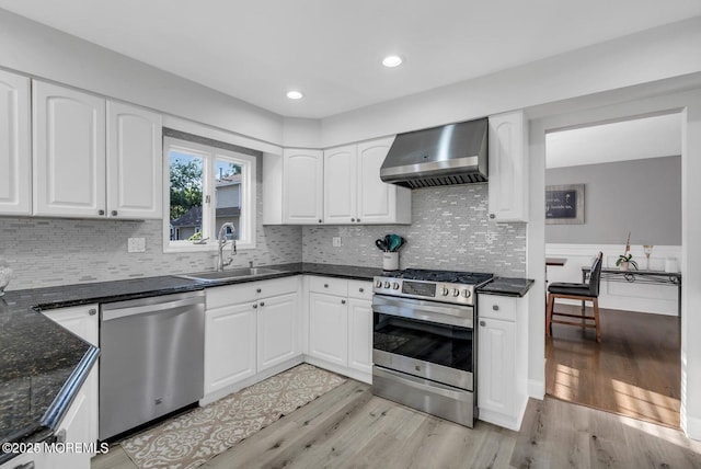 kitchen with white cabinetry, sink, light hardwood / wood-style floors, stainless steel appliances, and wall chimney exhaust hood