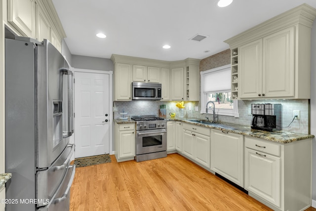 kitchen with light stone counters, stainless steel appliances, tasteful backsplash, light wood-type flooring, and sink