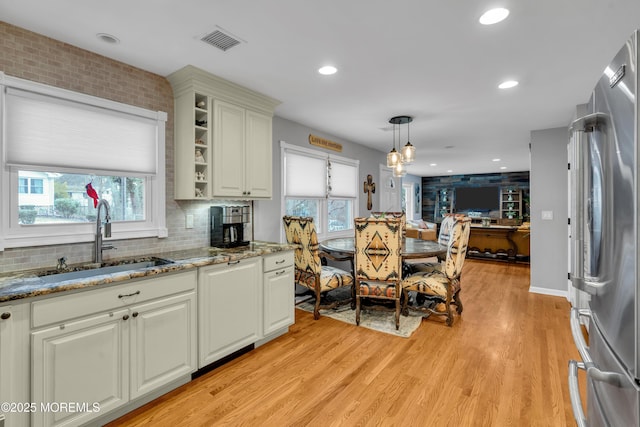 kitchen with light hardwood / wood-style floors, light stone countertops, stainless steel fridge, sink, and decorative light fixtures