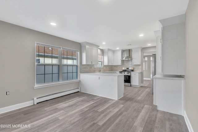 kitchen with white cabinets, wall chimney range hood, baseboard heating, and stainless steel range with gas stovetop