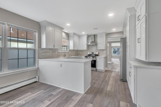 kitchen with white cabinets, stainless steel appliances, a baseboard radiator, and wall chimney range hood