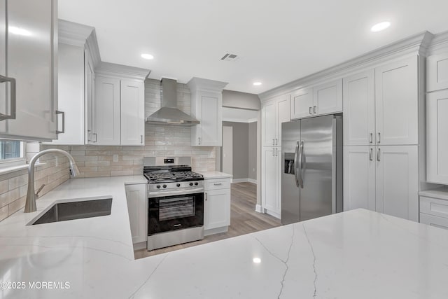 kitchen with light stone countertops, sink, wall chimney range hood, and appliances with stainless steel finishes