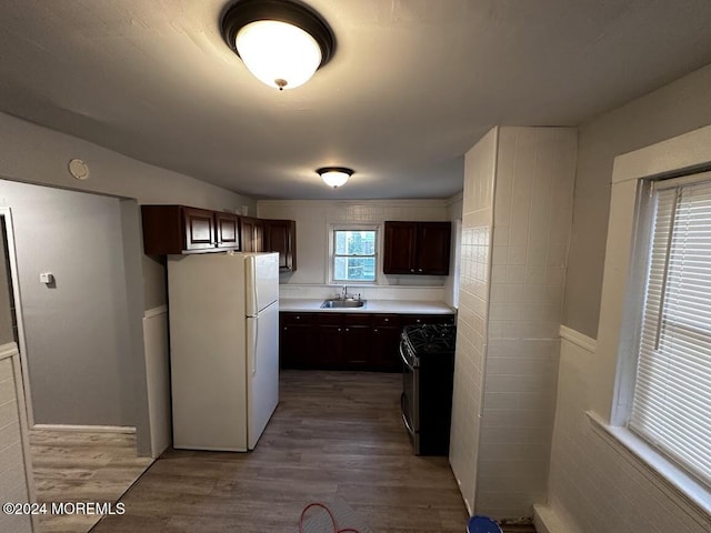 kitchen featuring dark brown cabinetry, sink, white refrigerator, wood-type flooring, and black range