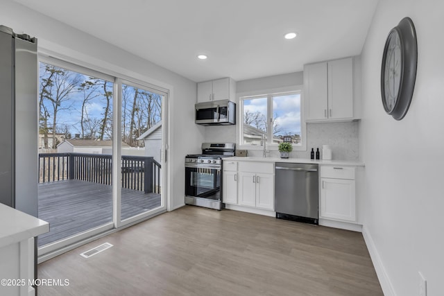 kitchen with appliances with stainless steel finishes, light wood-type flooring, backsplash, sink, and white cabinetry