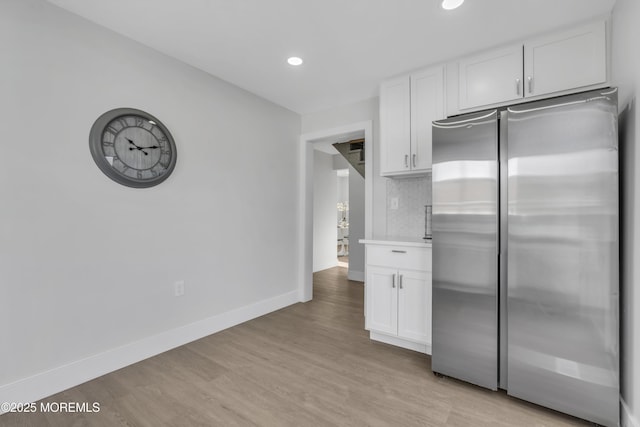 kitchen featuring backsplash, stainless steel refrigerator, white cabinets, and light wood-type flooring