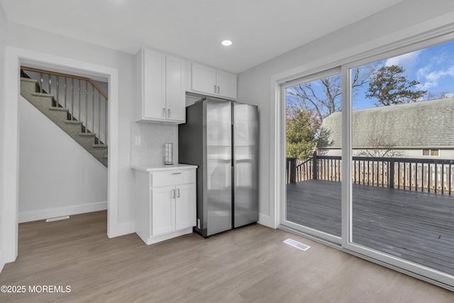 kitchen featuring stainless steel fridge, light wood-type flooring, white cabinetry, and tasteful backsplash