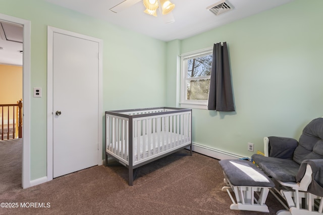 carpeted bedroom featuring a crib, baseboard heating, and ceiling fan