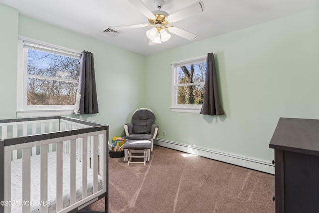 bedroom with a crib, baseboard heating, ceiling fan, and carpet floors