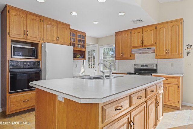 kitchen featuring sink, light tile patterned flooring, tasteful backsplash, an island with sink, and appliances with stainless steel finishes