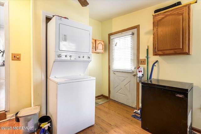 clothes washing area featuring cabinets, light wood-type flooring, and stacked washer and dryer