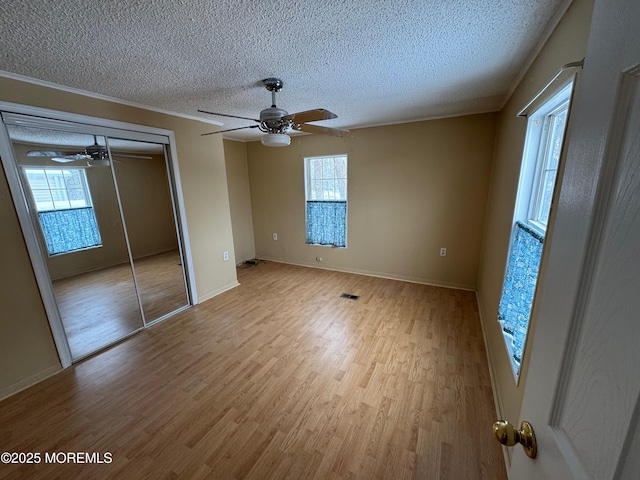 unfurnished bedroom featuring ceiling fan, a closet, a textured ceiling, and light wood-type flooring