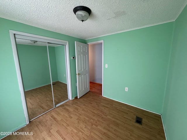 unfurnished bedroom featuring crown molding, a closet, light hardwood / wood-style floors, and a textured ceiling