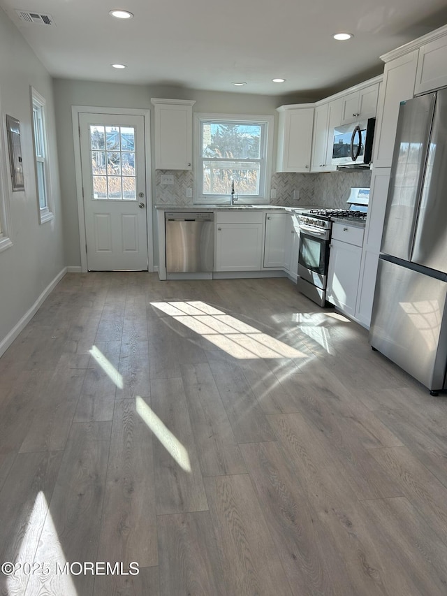 kitchen with stainless steel appliances, white cabinetry, and light hardwood / wood-style flooring