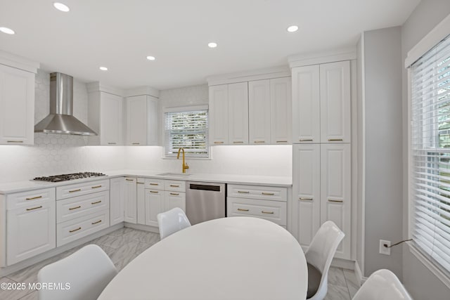 kitchen featuring stainless steel appliances, wall chimney range hood, backsplash, white cabinets, and sink