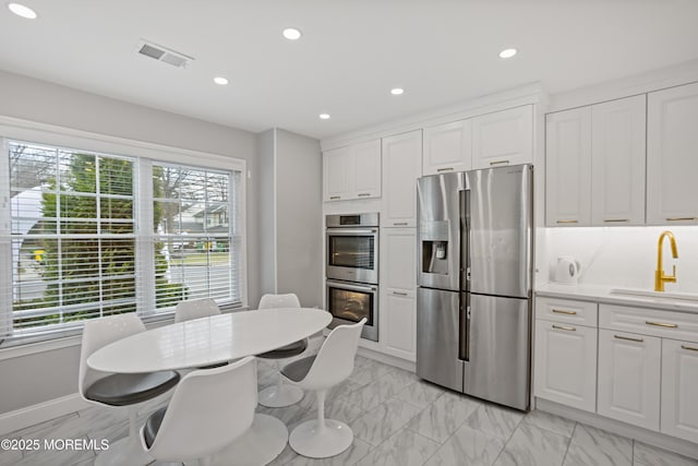 kitchen with appliances with stainless steel finishes, white cabinetry, a wealth of natural light, and sink