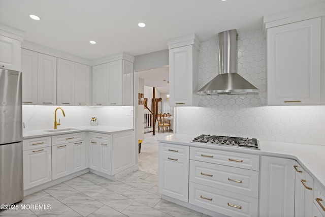 kitchen with stainless steel appliances, wall chimney range hood, decorative backsplash, white cabinets, and sink