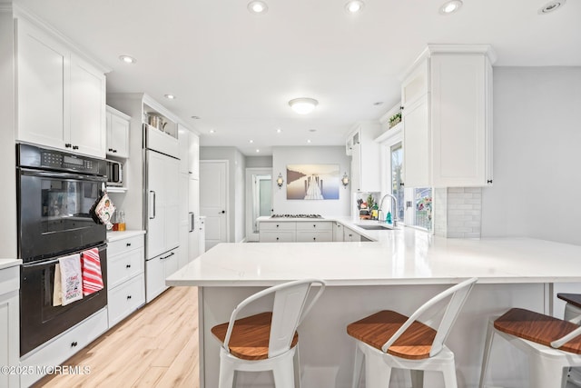 kitchen with kitchen peninsula, sink, double oven, a kitchen bar, and white cabinetry